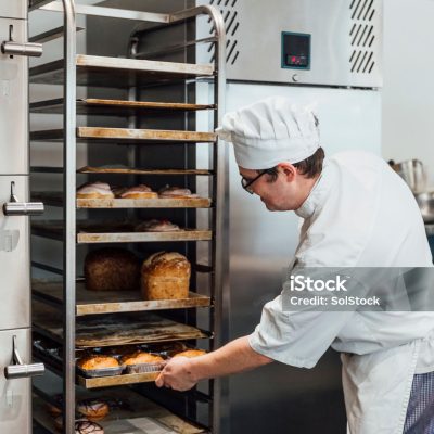 A young baker filling up the shelves with orders for the day in the family ran bakery.